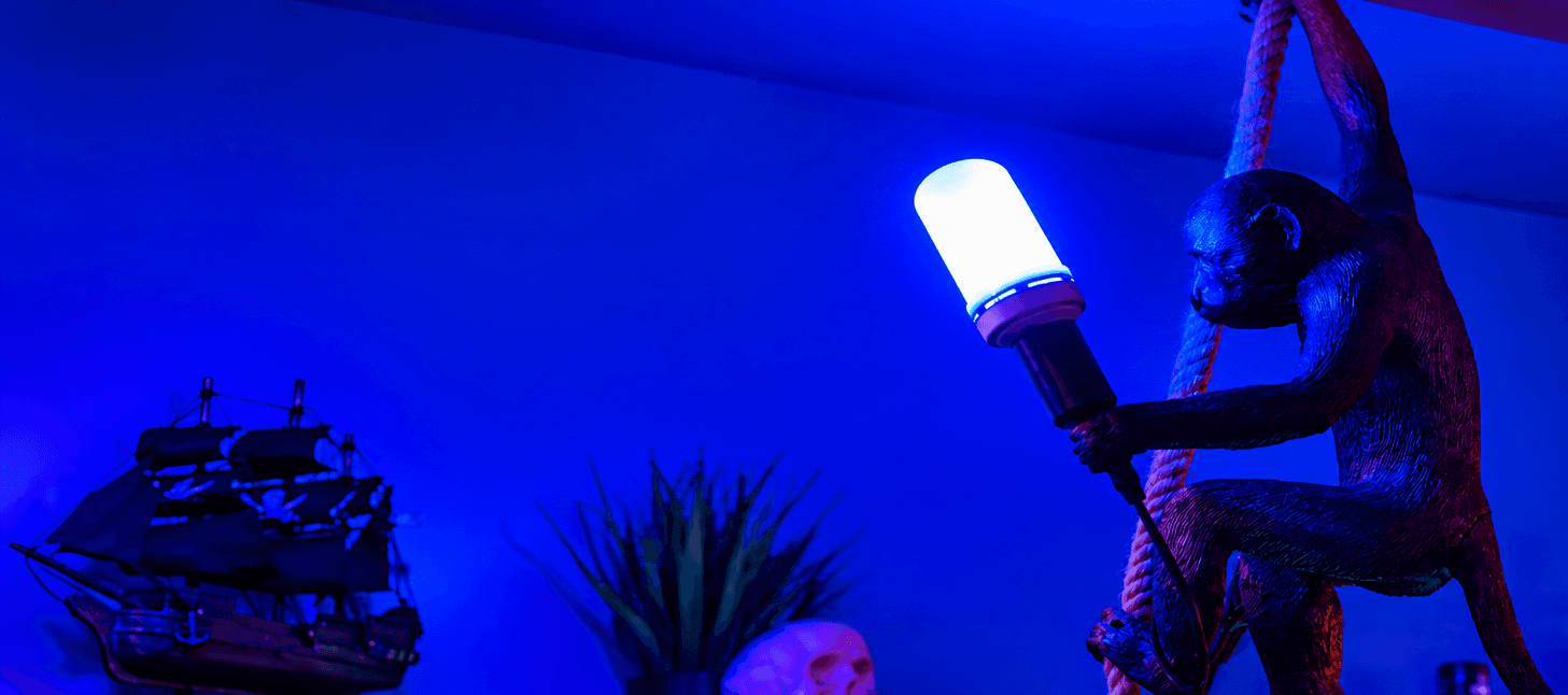 Monkey statue hanging from a rope holding a glowing blue light bulb in blue lighting.