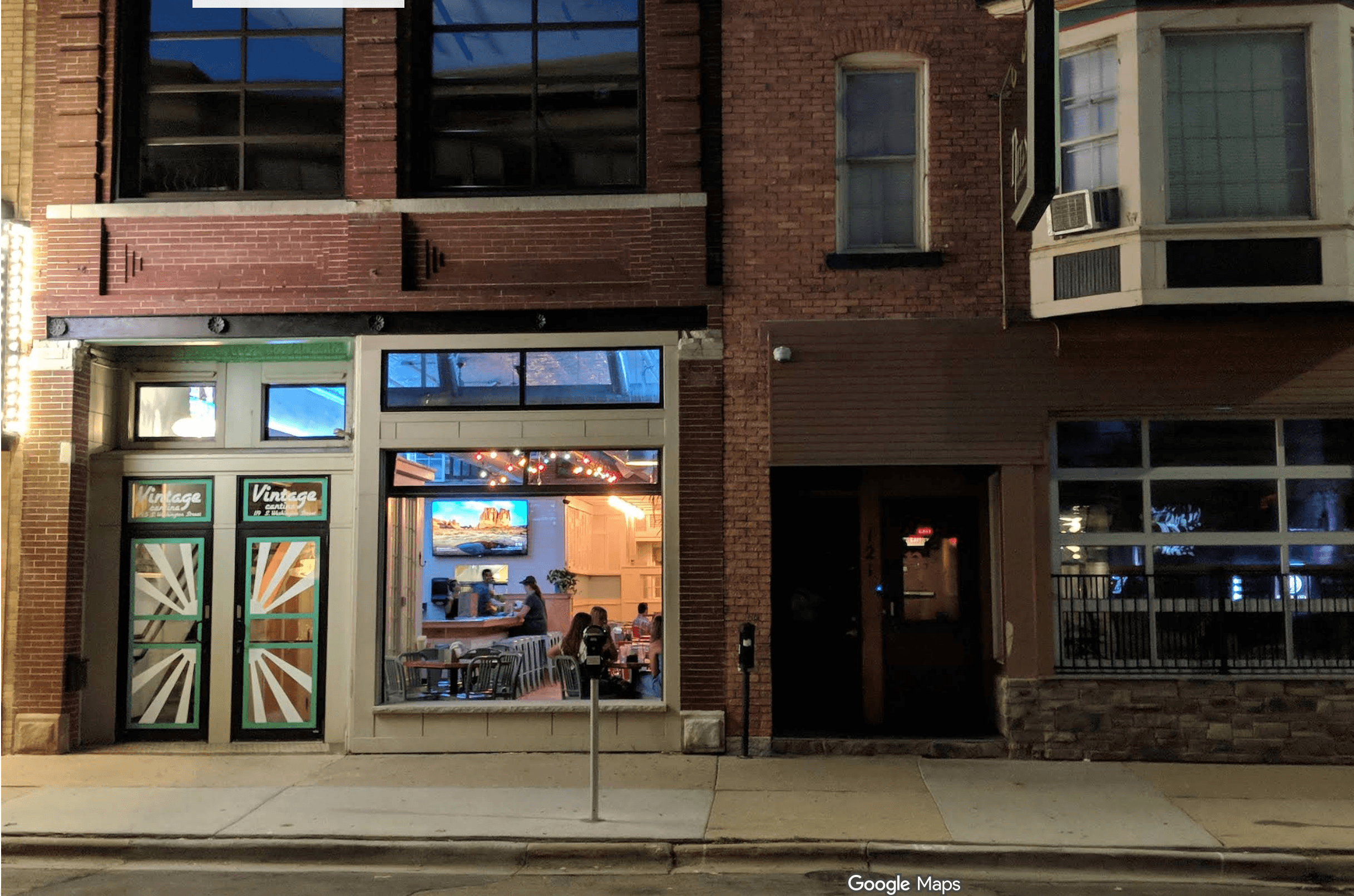 Brick storefront of Vintage Cantina at night with patrons visible through a large glowing window.