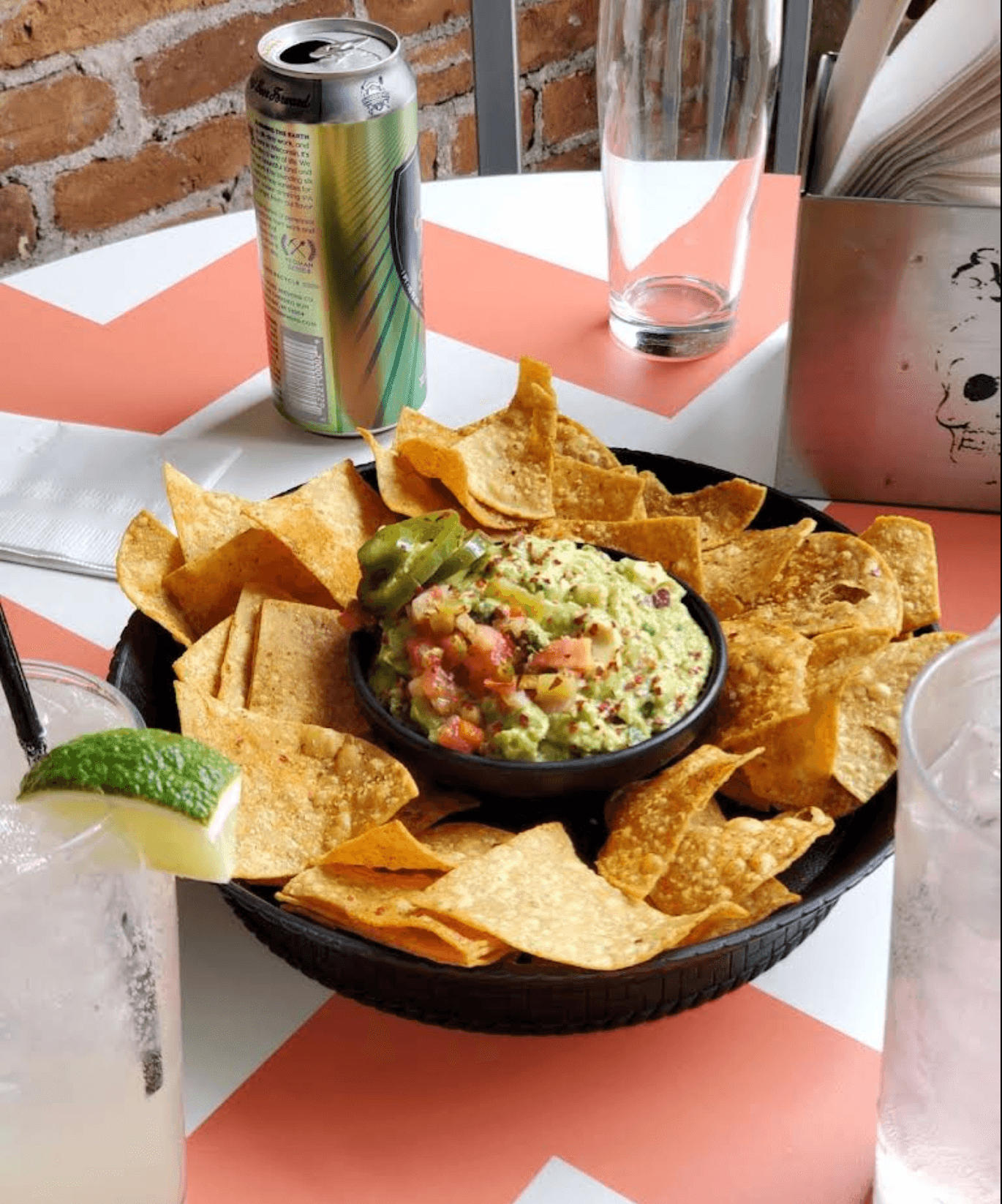 Tortilla chips and fresh guacamole on a chevron-patterned table with a cocktail and beer.