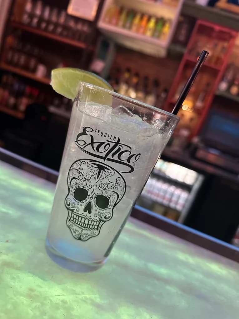 Exotico tequila cocktail with ice and lime in a sugar skull glass at a bar.